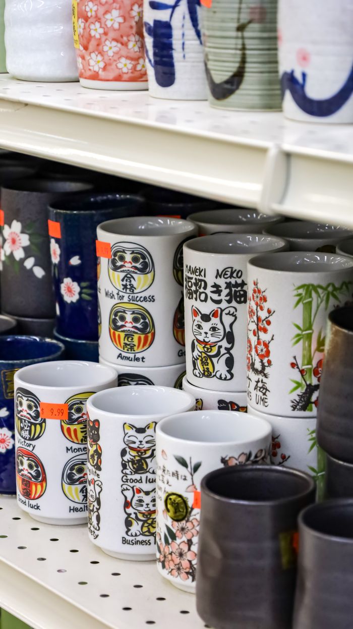 A display of ceramic mugs featuring Japanese Lucky Cat designs on a store shelf.